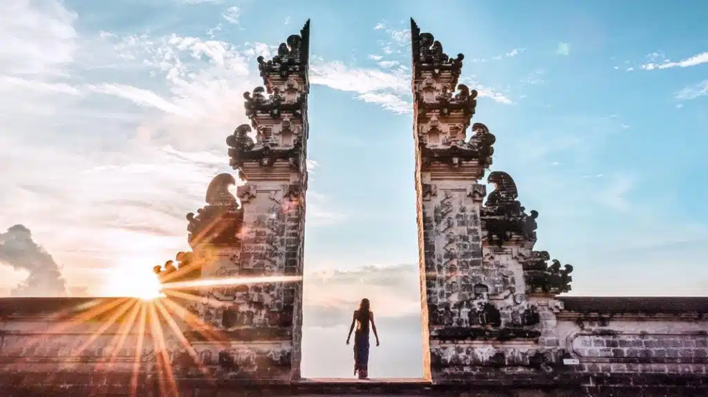 A person standing at the Lempuyang Temple gateway with the sun rising in the background.