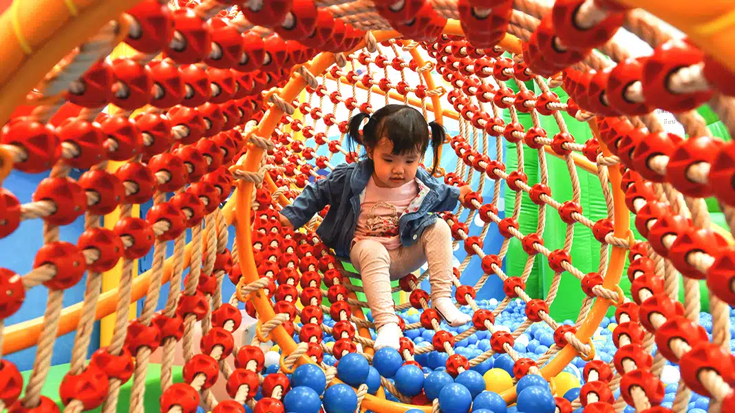 child plays in a colorful ball pit tunnel at Peek A Boo Kids Playground.