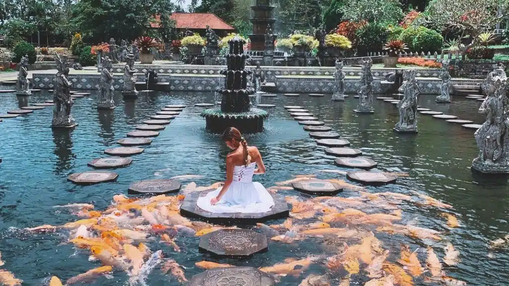 A visitor surrounded by koi fish at Tirta Gangga Water Palace in Bali.