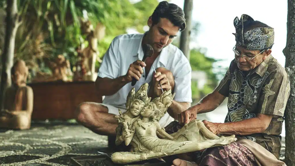 Master and apprentice wood carvers shape a sculpture in Bali.